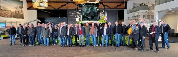 Gruppe von Männern in Arbeitskleidung vor einem Traktor in einem Ausstellungsraum.