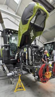 Traktor mit geöffnetem Motorraum in einer Werkstatt. Mechaniker bei der Arbeit.