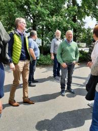 Gruppengespräch im Freien, mehrere Personen in lockerer Kleidung, Bäume im Hintergrund.
