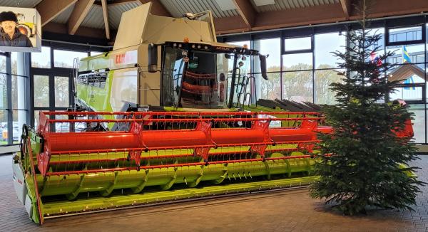 Eine bunte Erntegeräte-Maschine steht in einem modernen Raum neben einem Weihnachtsbaum.